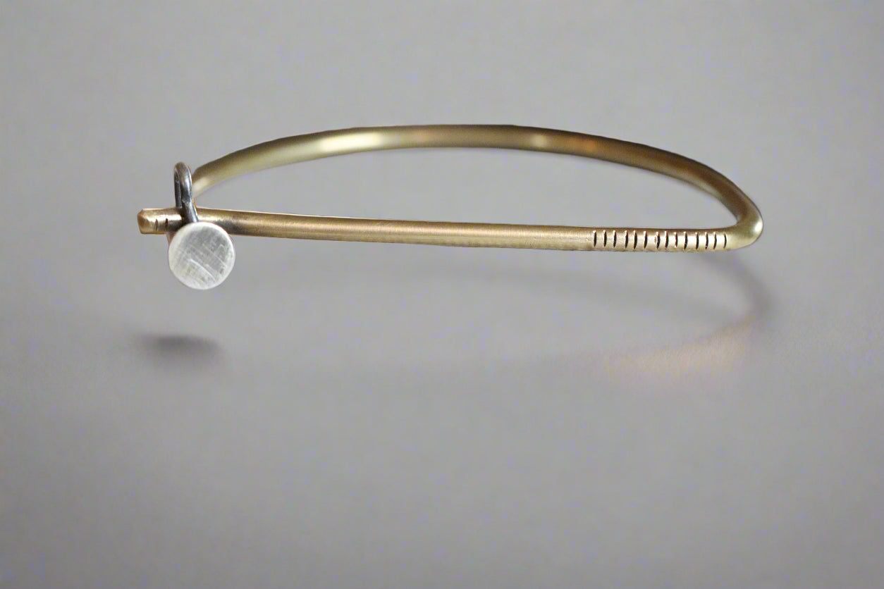 Gold bracelet with a round charm on a textured white surface