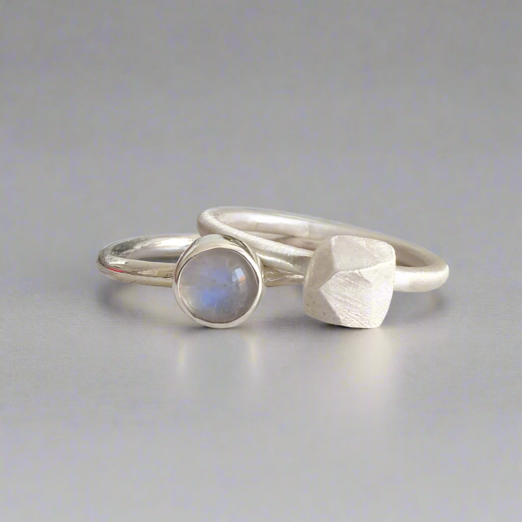 Two silver rings with gemstones on a light gray surface moonstone