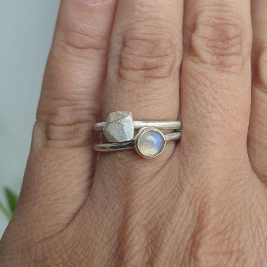 Two silver rings with gemstones on a person's finger against a neutral background