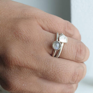 Close-up of a hand wearing two silver rings with gemstones on a neutral background